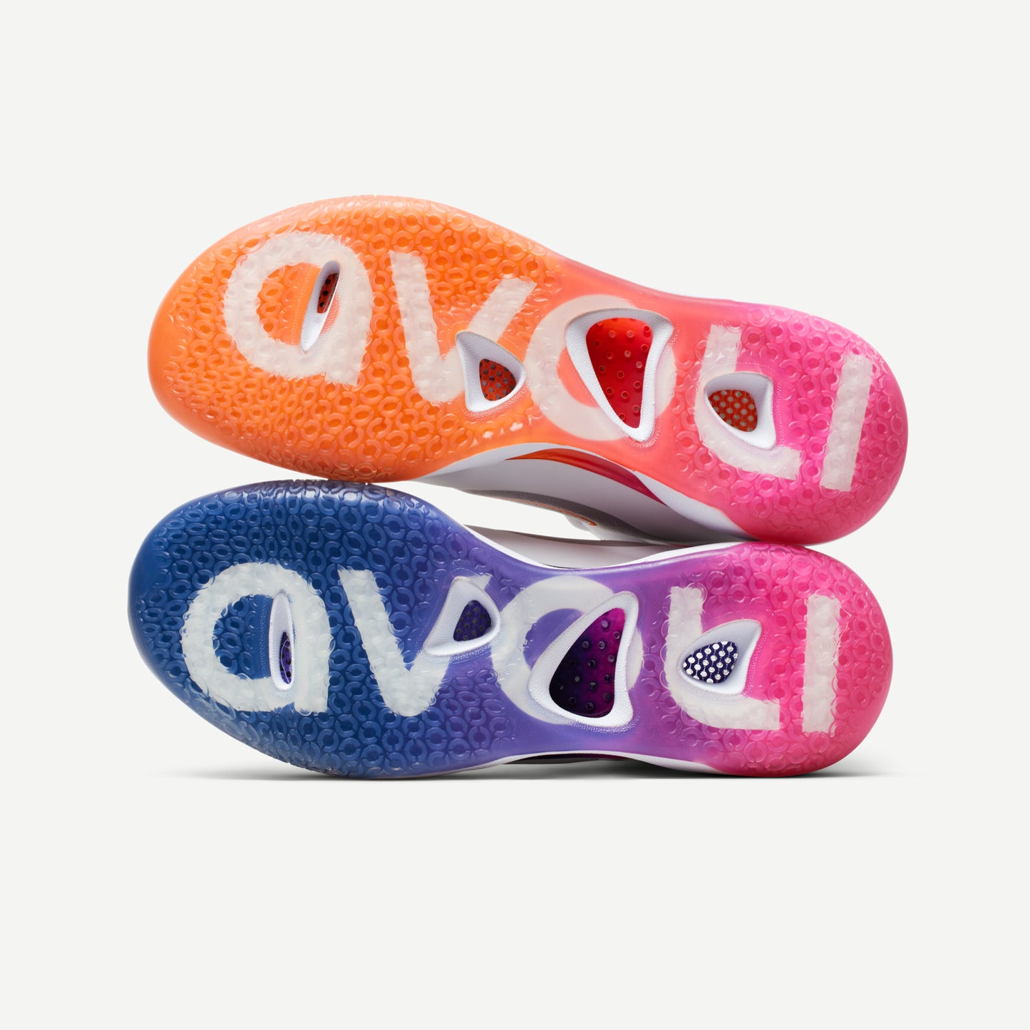 The soles of a pair of mismatched Avoli Low volleyball shoes with white as the primary color and blue, orange, and pink details.