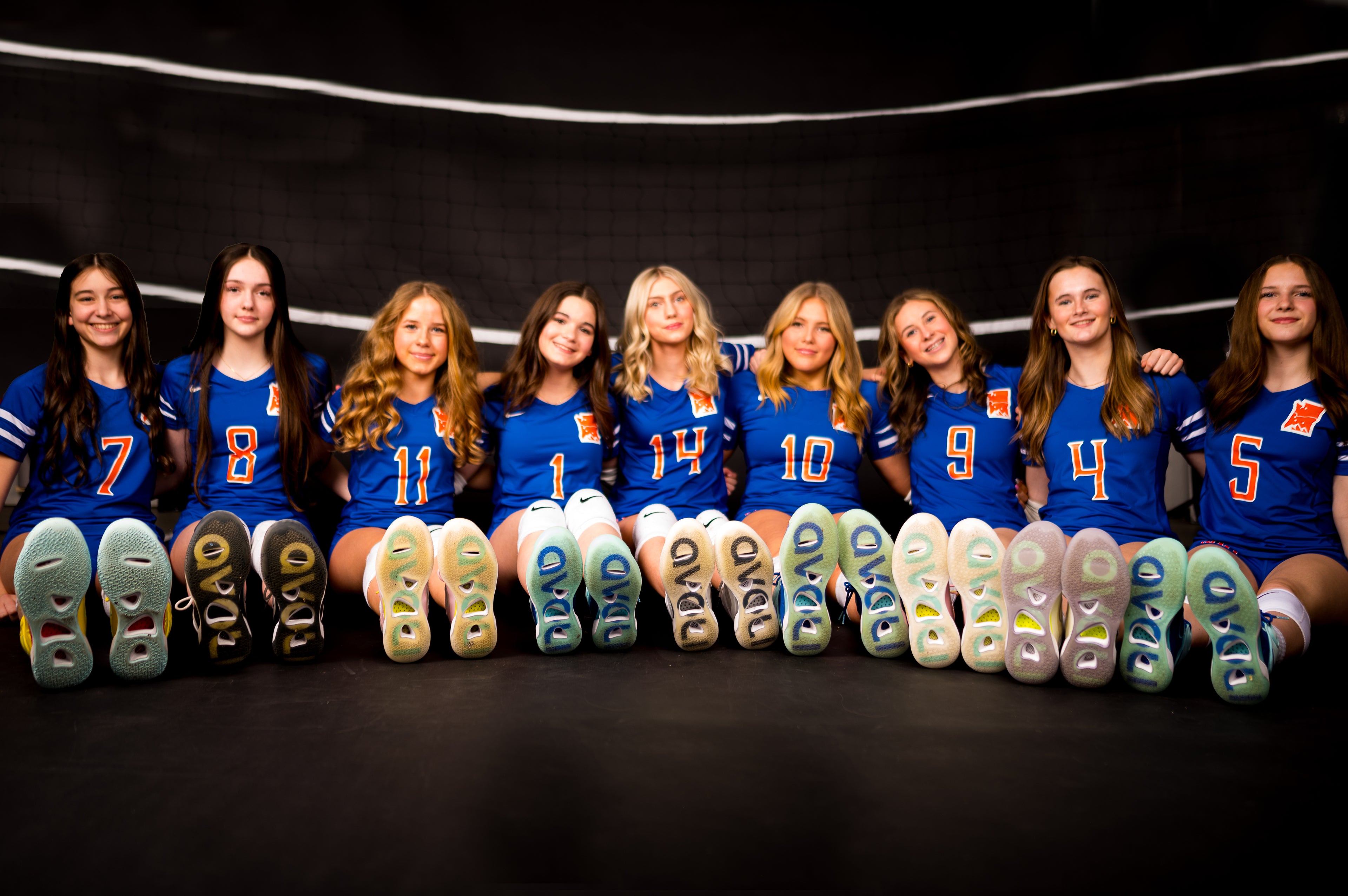 Group of women in blue sports jerseys with visible numbers posing together showing their Avoli volleyball sneakers